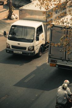 Aerial view of urban street with trucks and scooter riders, showcasing daily city life.