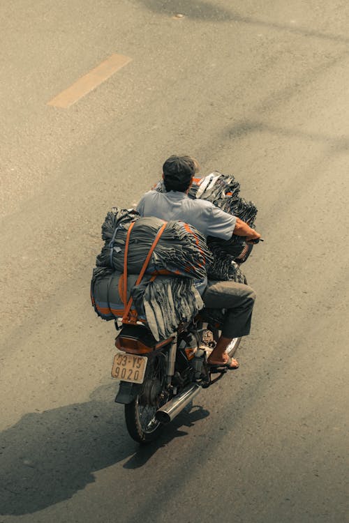 High Angle Shot of a Man Riding on a Motorcycle with a Stack of Items 