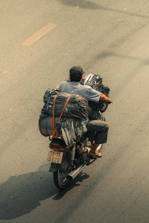 Free Man riding a heavily loaded motorcycle on a sunny city street with visible license plate. Stock Photo