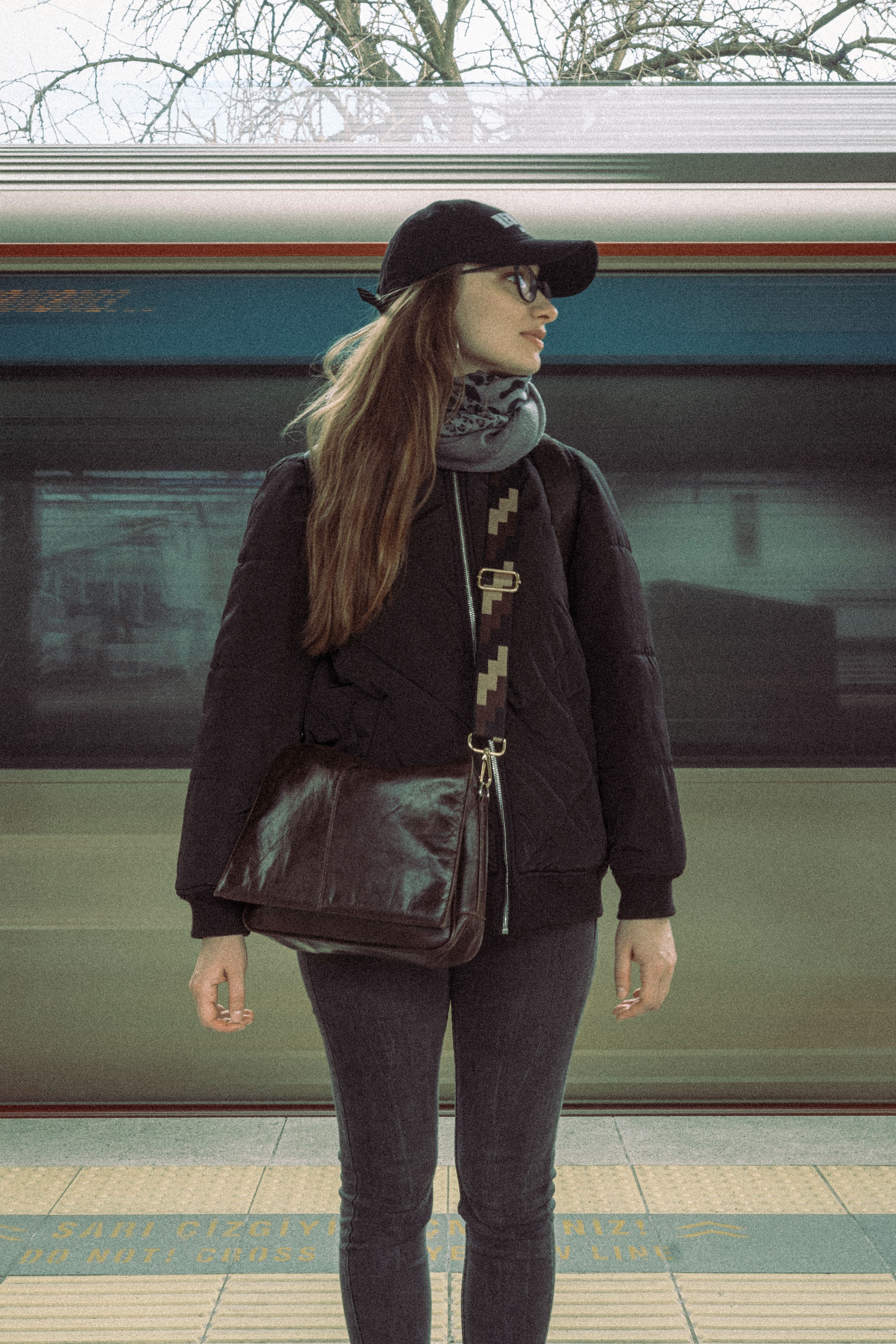 A stylish woman in casual attire waits at a bustling railway station, embodying modern travel culture.