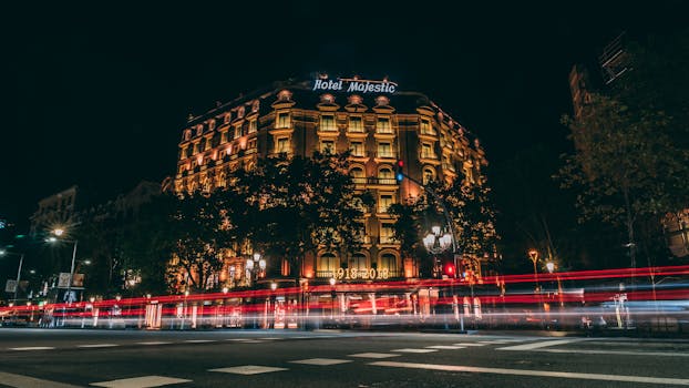 Illuminated Hotel Majestic in Barcelona captured at night with vibrant light trails.