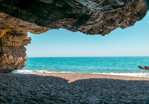 Free Peaceful beach view through a rocky cave opening with turquoise ocean waves under a clear blue sky. Stock Photo