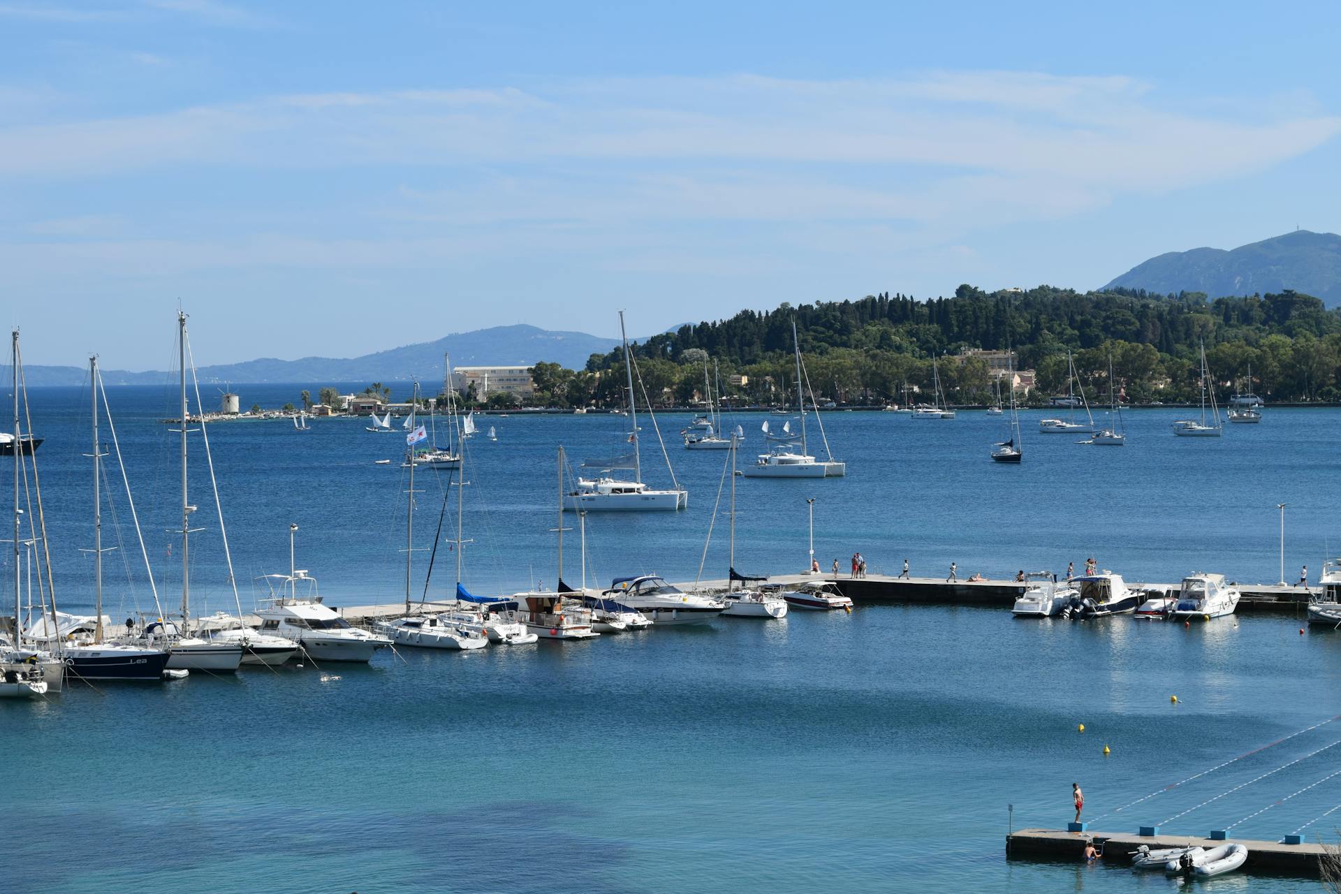 Stunning view of a marina in Corfu, Greece with yachts anchored and a scenic island backdrop.