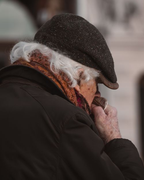 Free Senior man with gray hair wearing an ivy cap and scarf, blowing nose on a winter day in Stockholm. Stock Photo