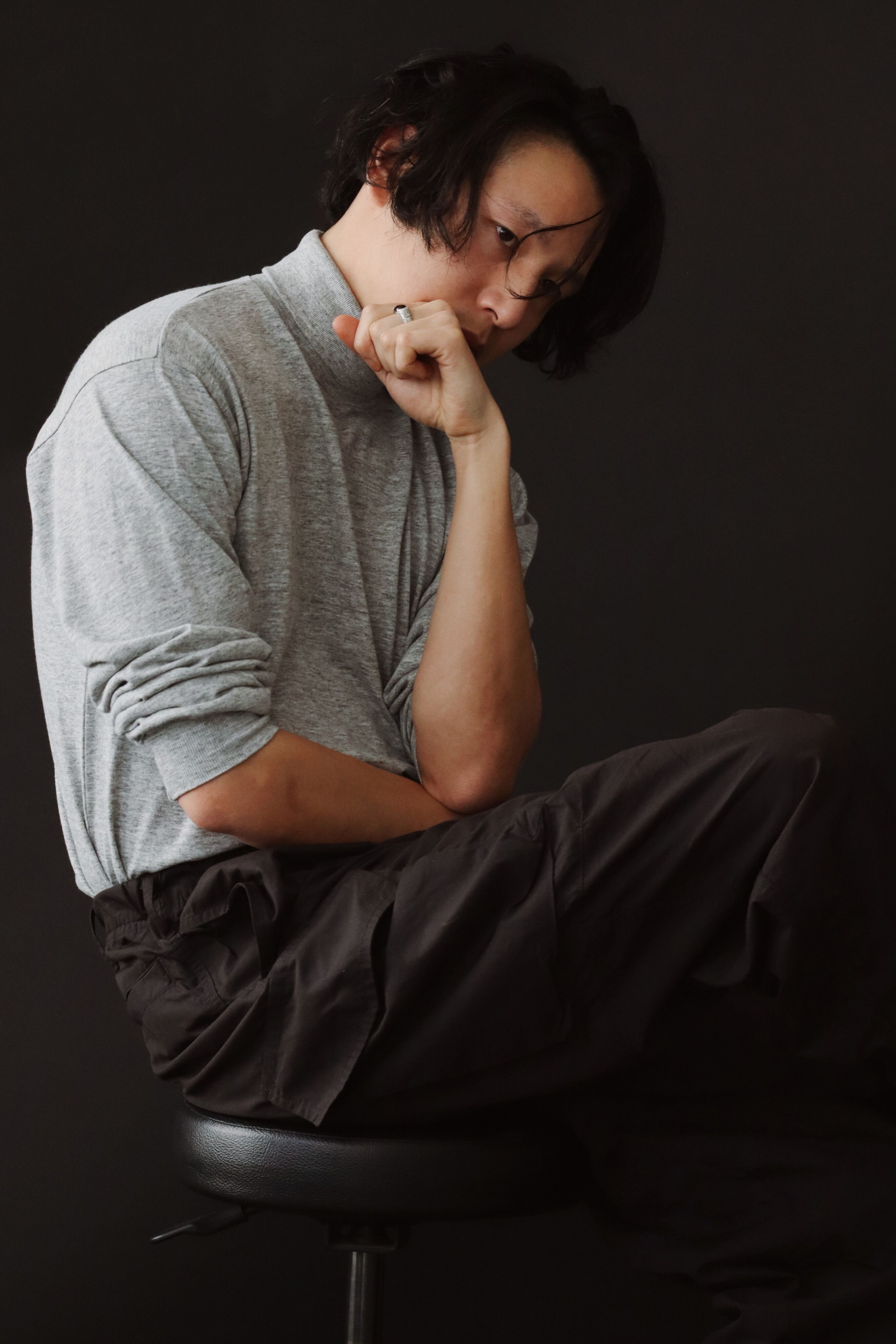 Portrait of a stylish man in Berlin studio, lost in thought against a dark backdrop.
