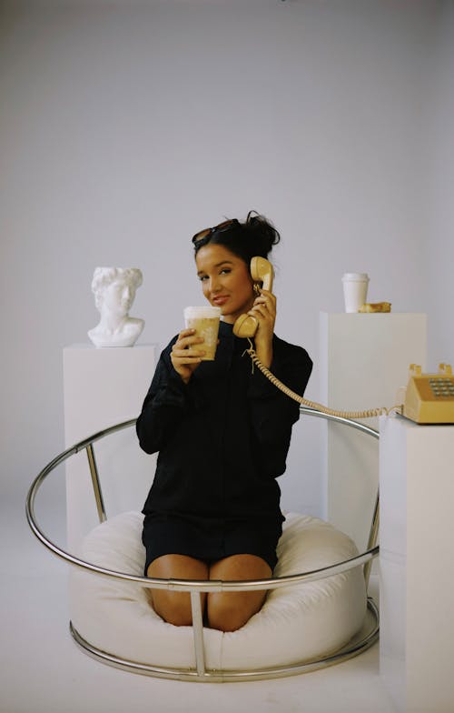 A woman sitting on a chair with a phone and a cup of coffee