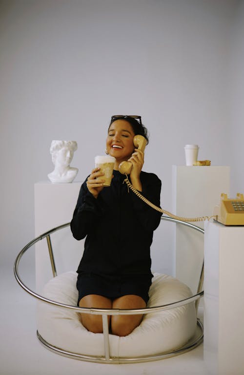 Smiling Brunette Woman Kneeling on Beanbag and Holding Telephone Handset