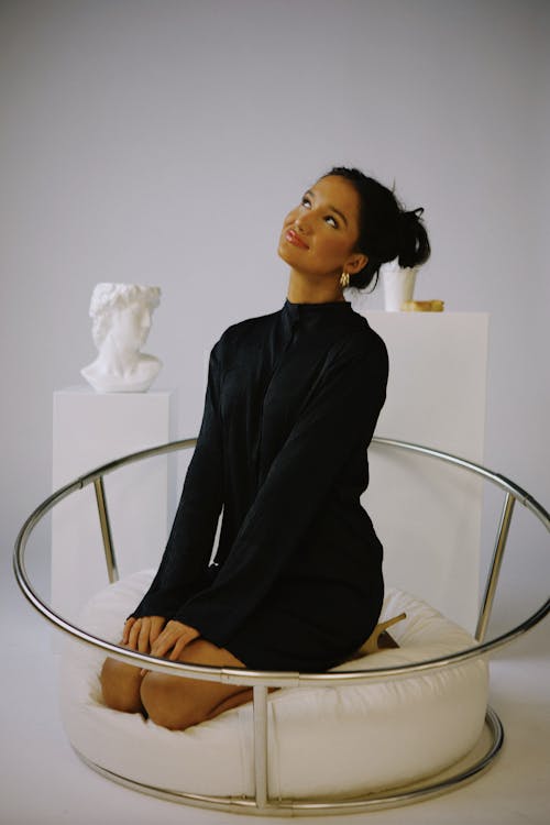 A woman sitting on a white chair with a white background