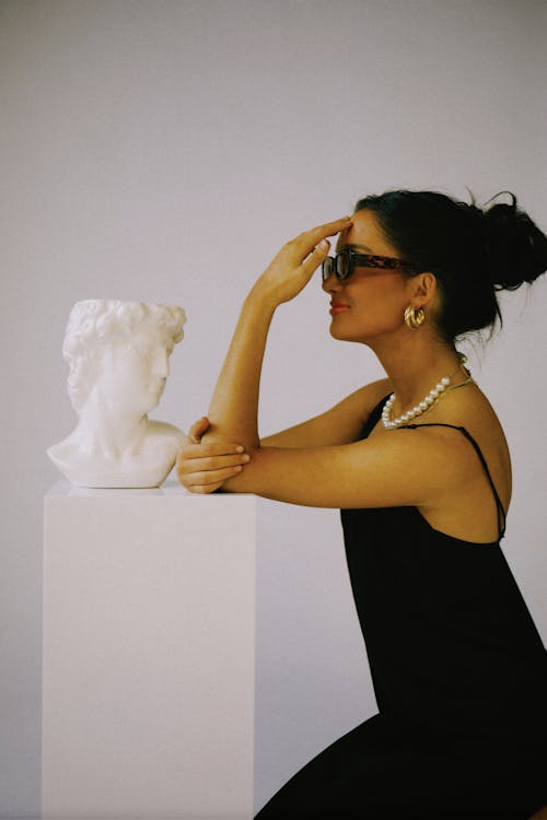 Brunette Woman in Sunglasses and Black Dress Leaning on Stand with Bust