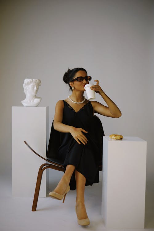 Brunette Woman in Black Dress Sitting and Drinking