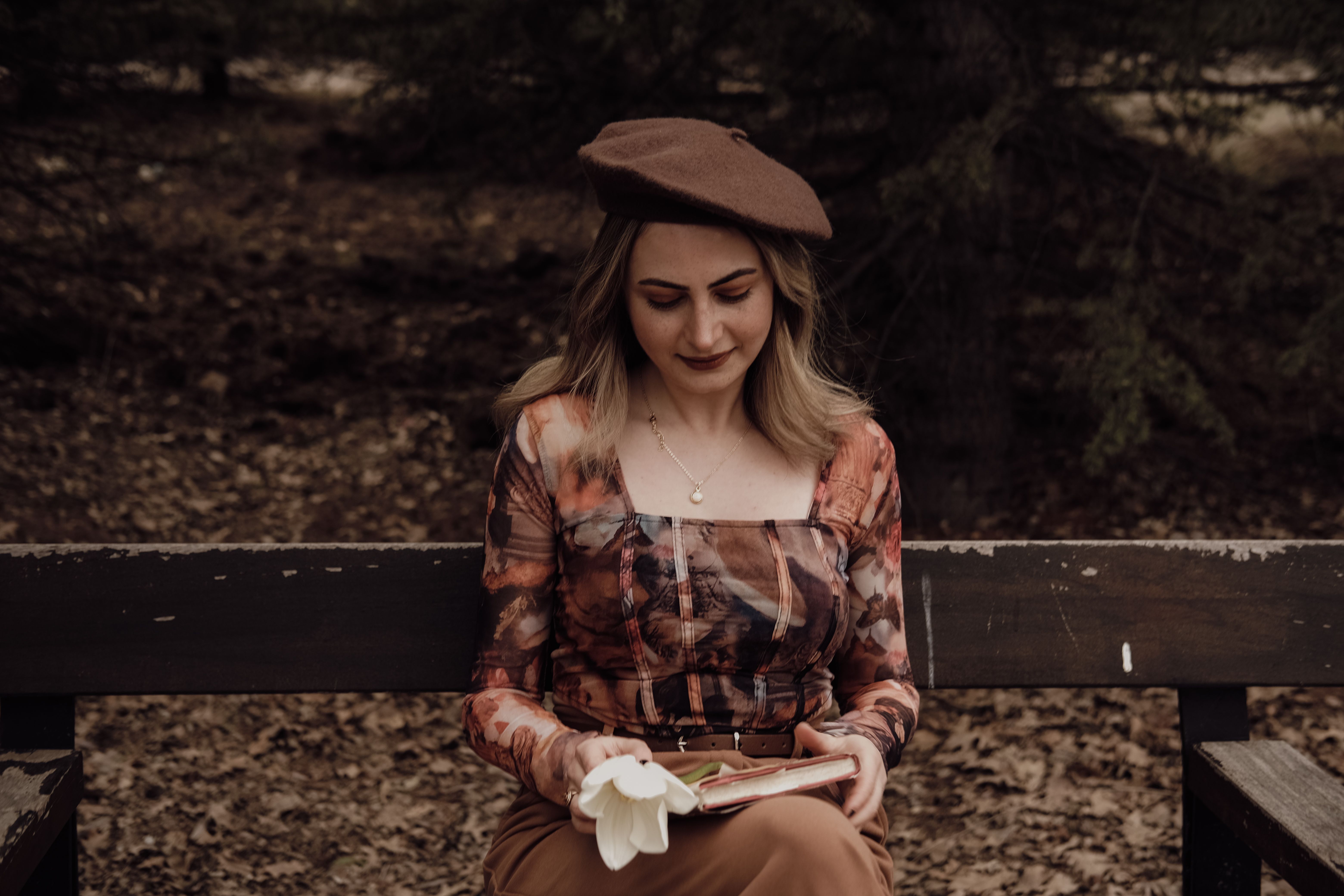 A person sitting on a park bench looking at a book instead of a phone, surrounded by autumn leaves