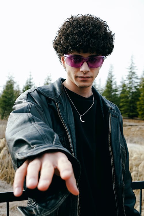 A man with sunglasses and a purple jacket pointing at something