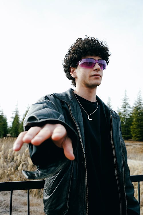 A man with curly hair and sunglasses is pointing at something
