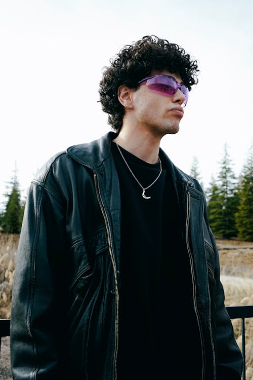 A man with curly hair wearing a leather jacket and sunglasses