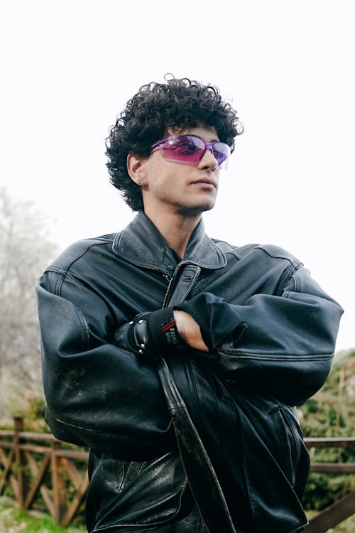 A man with curly hair and sunglasses is posing