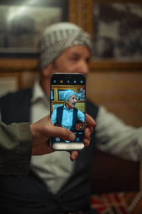 Person Hand Holding Smartphone and Taking Pictures of Elderly Man