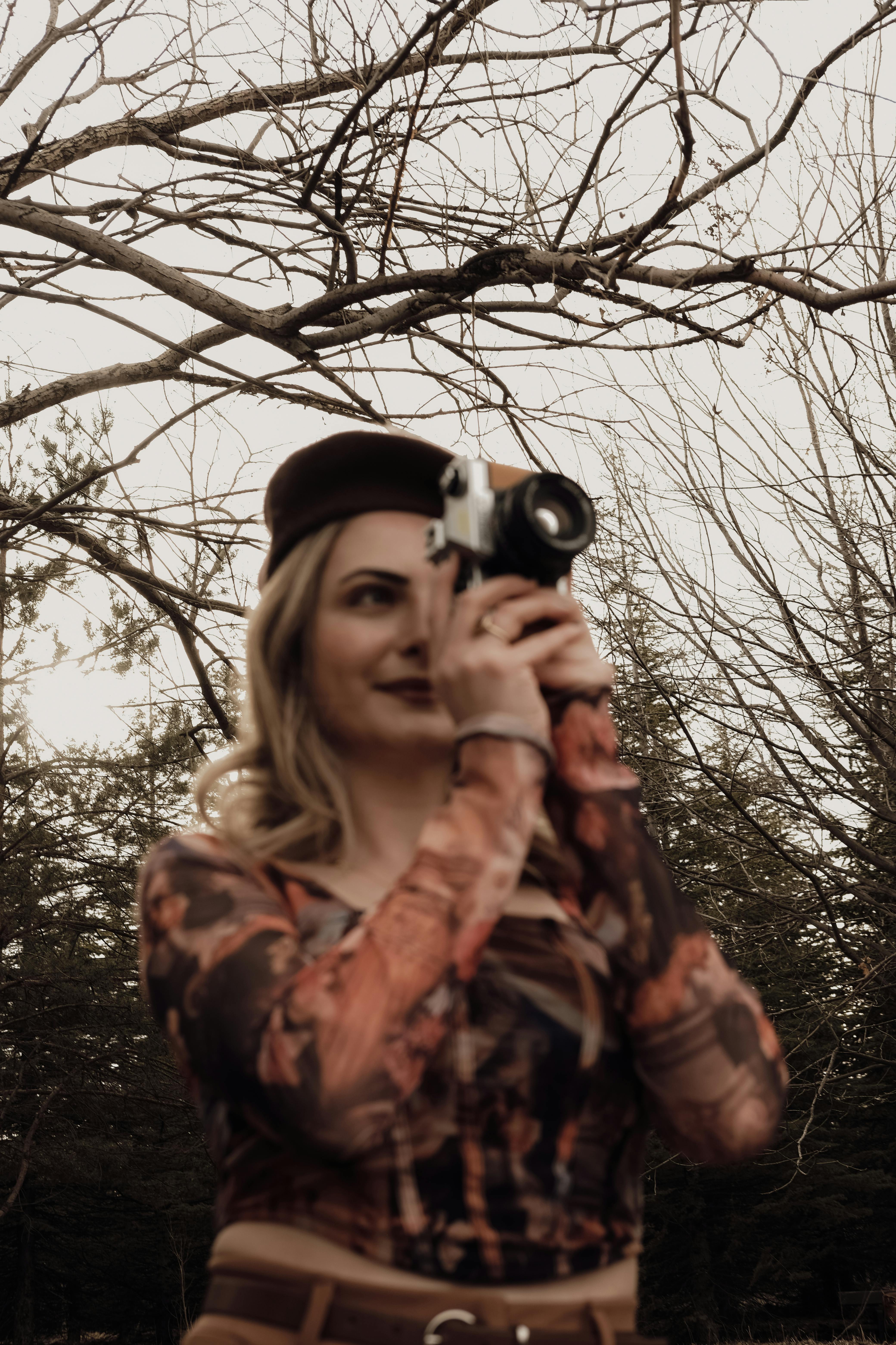 A woman holding a vintage camera, capturing moments in a scenic park during a spring day.