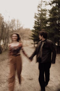 A couple holding hands running through a forest, captured with blurred motion.