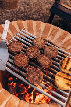 Close-up of sizzling beef burgers grilling over open flame on a brick barbecue.