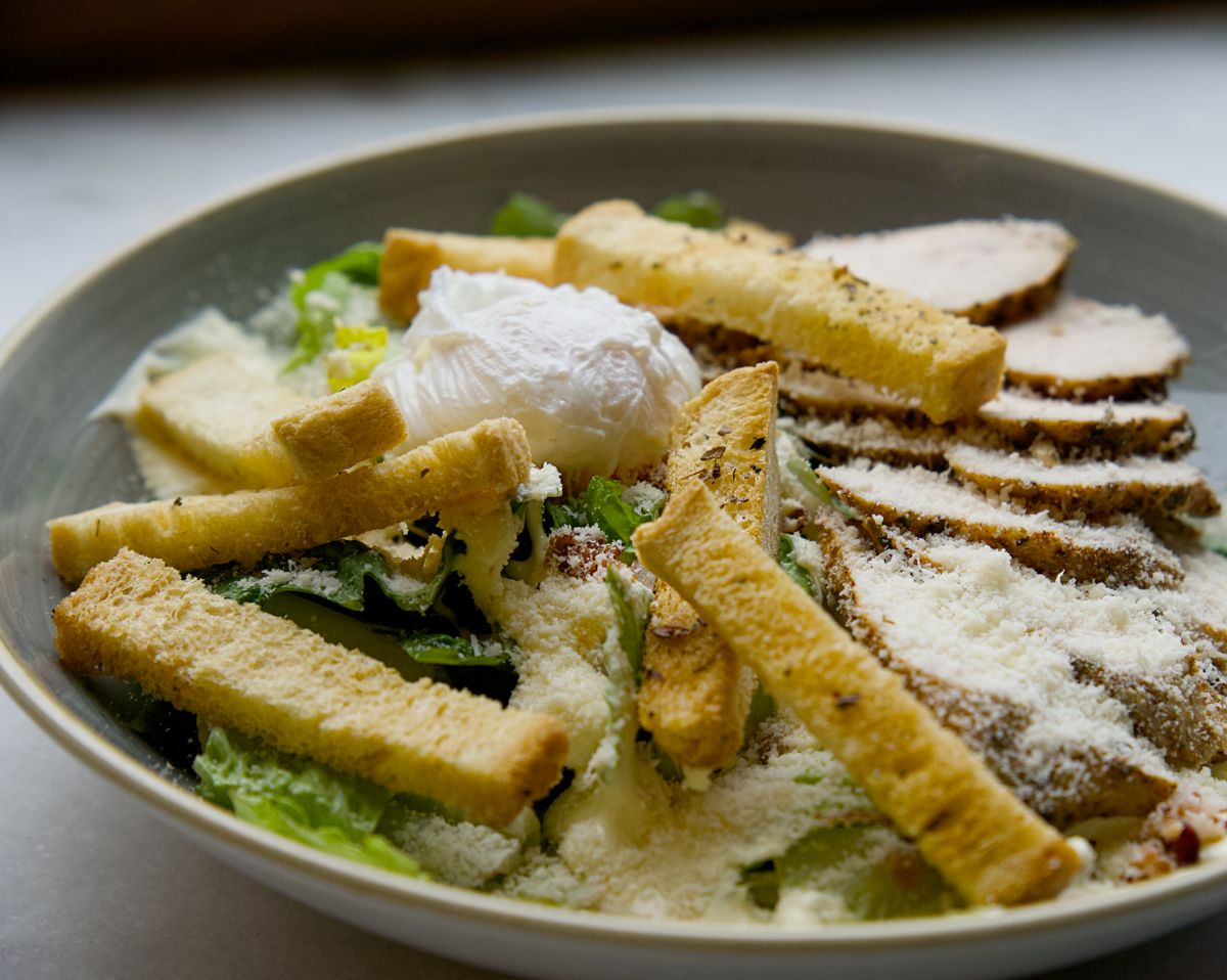 Caesar salad with sliced roast chicken, poached egg, long croutons and grated parmesan