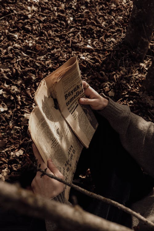 A Person Sitting on the Ground with a Newspaper 