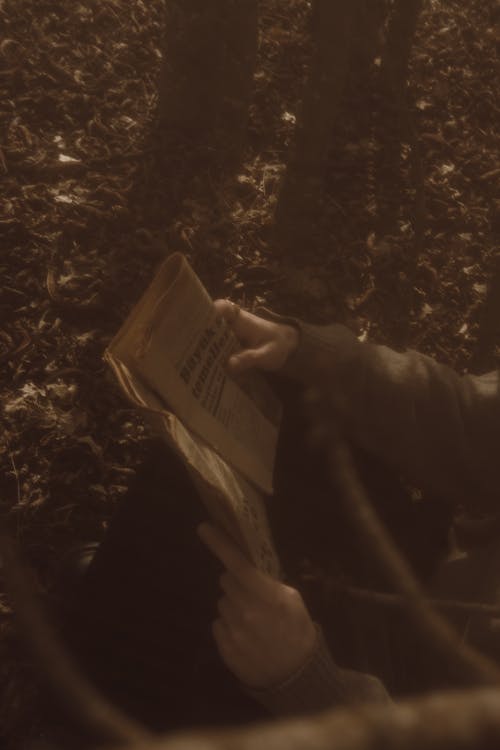 Sepia Toned Photo of a Person Sitting on the Ground with a Newspaper 