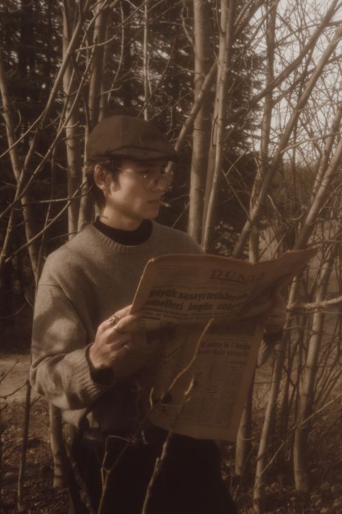 Free Man in vintage attire reading a newspaper outdoors in a rural area, evoking a historic and serene atmosphere. Stock Photo