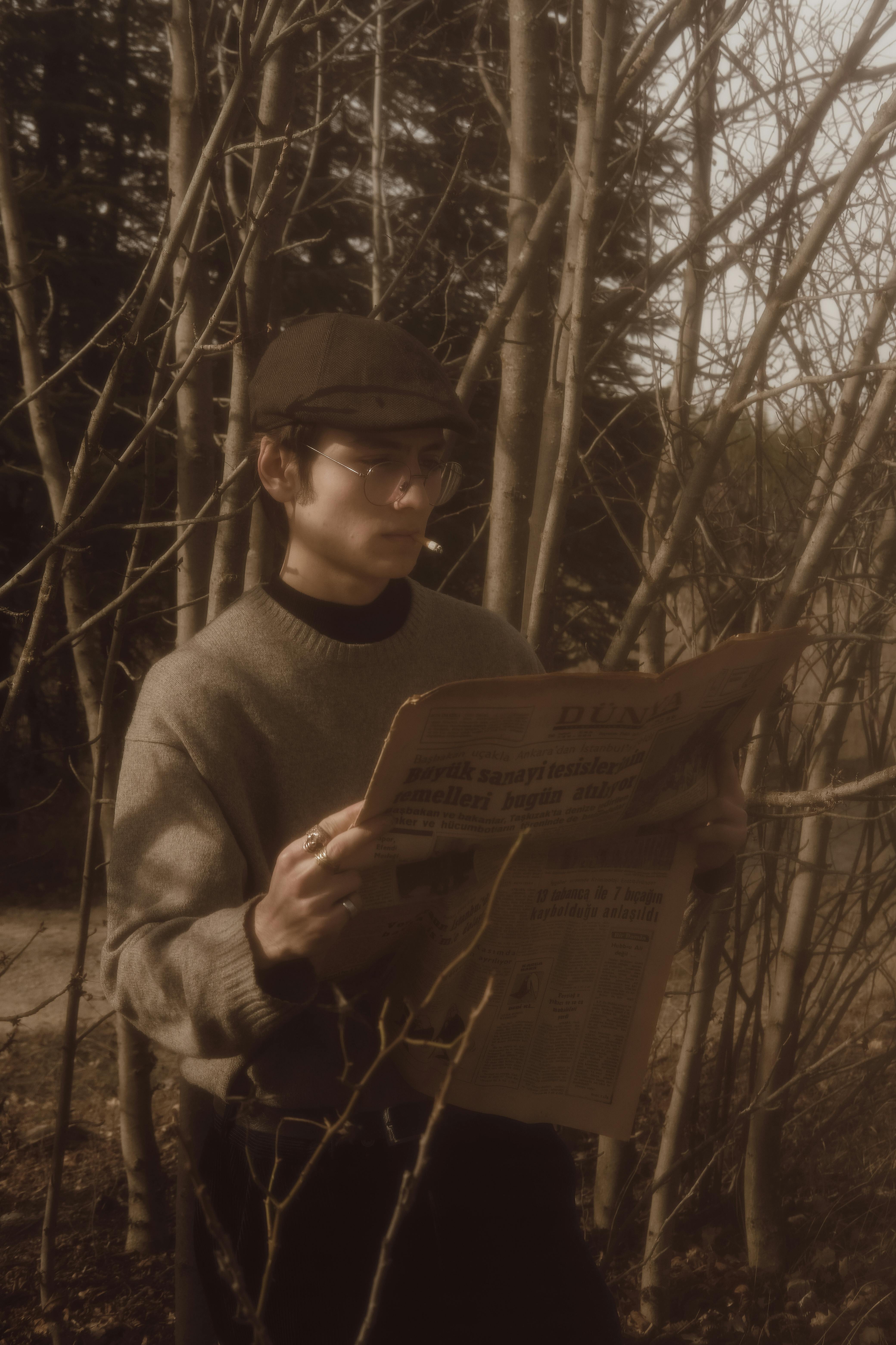 Young man in a retro outfit reading a newspaper outdoors in a forest setting.