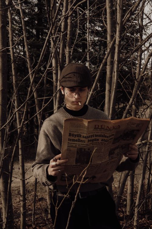 Free A young man reads a vintage newspaper in an autumn forest setting. Stock Photo