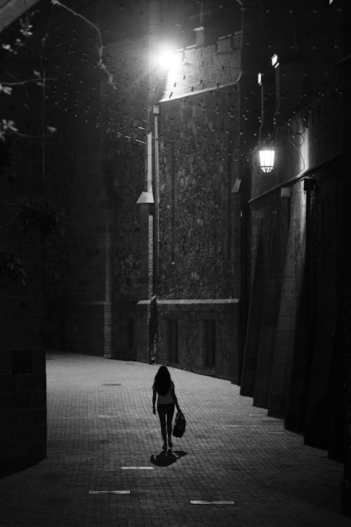 Black and White Back View of a Woman Walking on a Pavement at Night 
