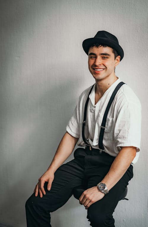 A man in suspenders and a hat sitting on a chair