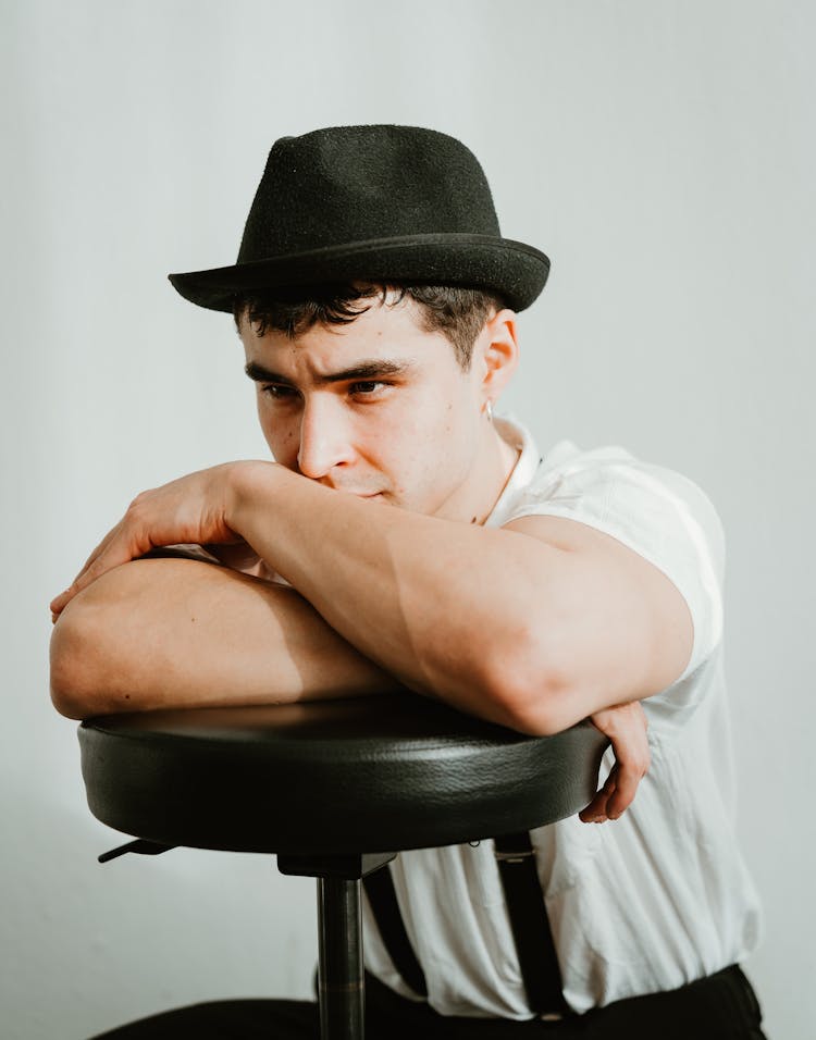 Young Man In Hat Sitting On Chair In Studio