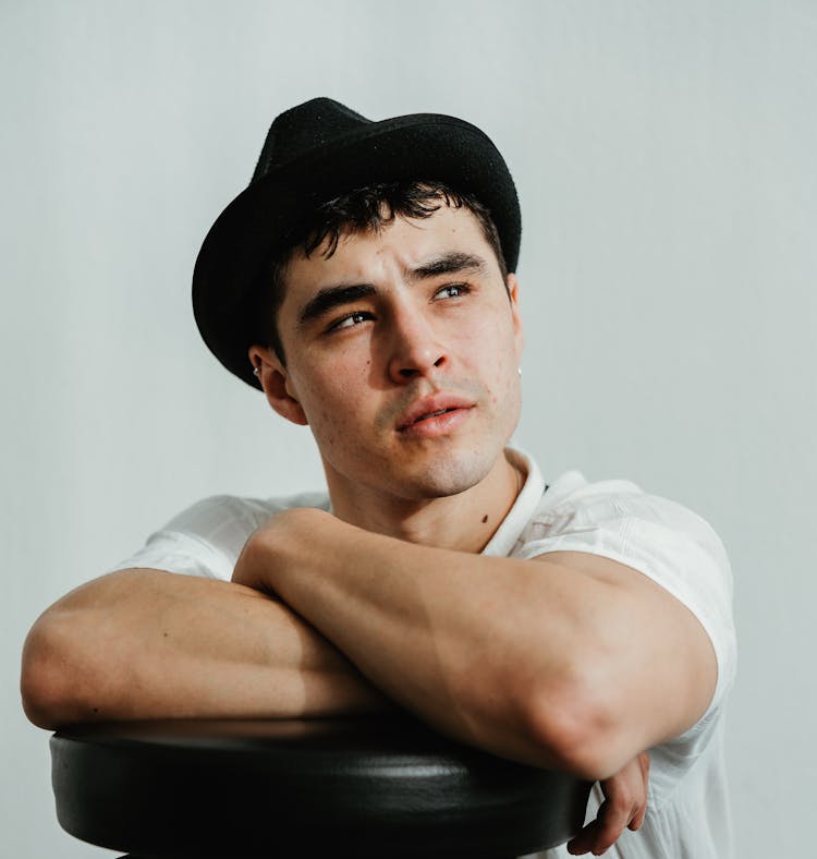 Young Man In Hat Sitting In Chair In Studio