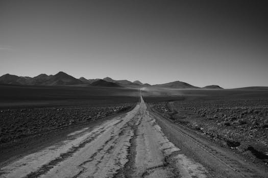 A black and white photo of a barren dirt road leading through the Bolívar District, revealing distant mountains.