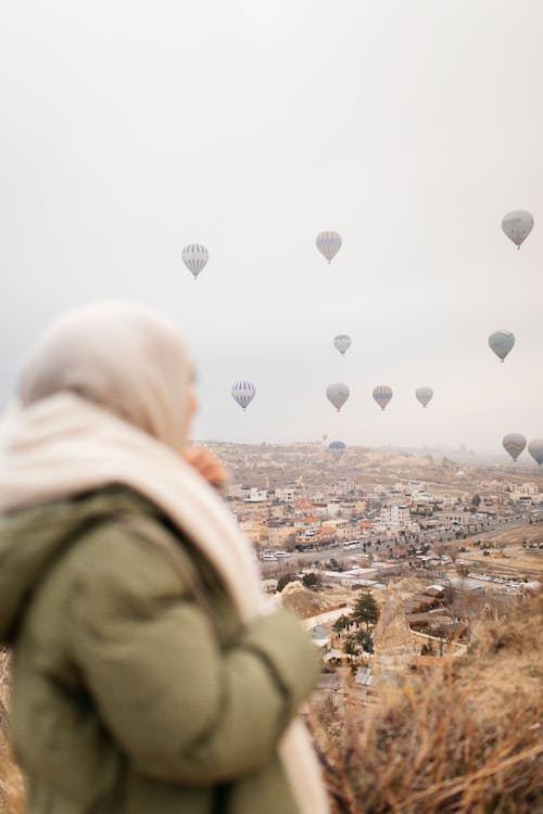 A woman in a green scarf looking at hot air balloons