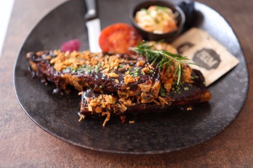 Free Close-up of a gourmet ribs dish topped with crispy onions and fresh herbs, served on a dark plate. Stock Photo