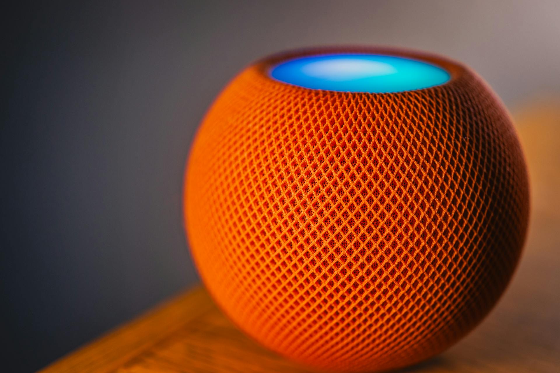 Close-up of an orange smart speaker with a glowing blue light, showcasing modern technology.