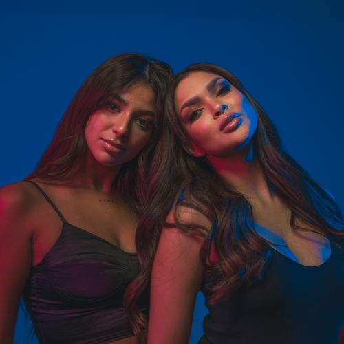 Free Dynamic portrait of two women posing with colorful studio lighting on a blue background. Stock Photo