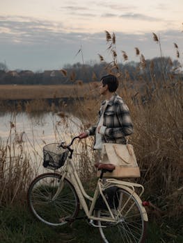A person with a bicycle enjoys a peaceful sunset by the lakeside, surrounded by nature.