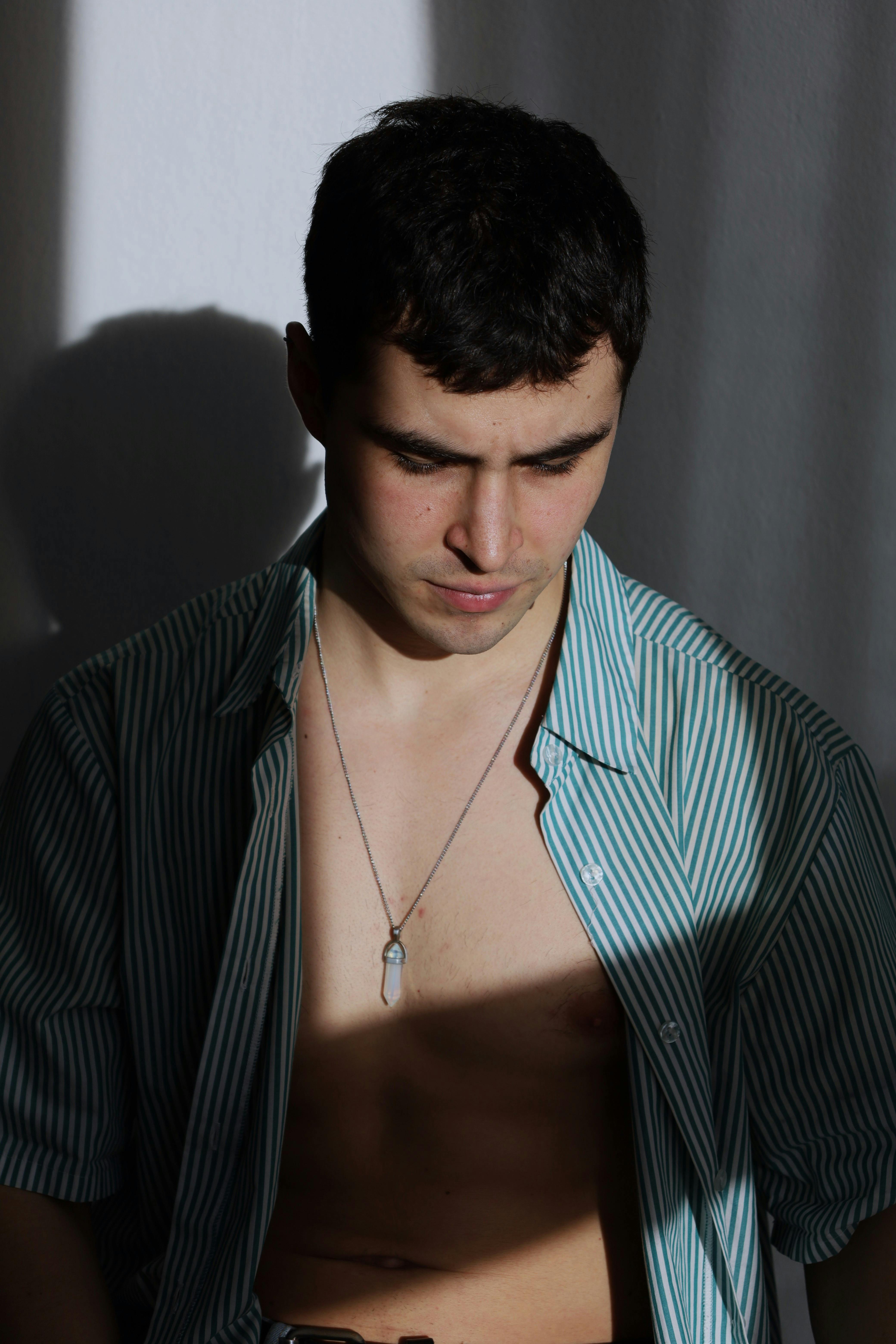 Portrait of a young man with shadows on his face, wearing an unzipped green shirt.