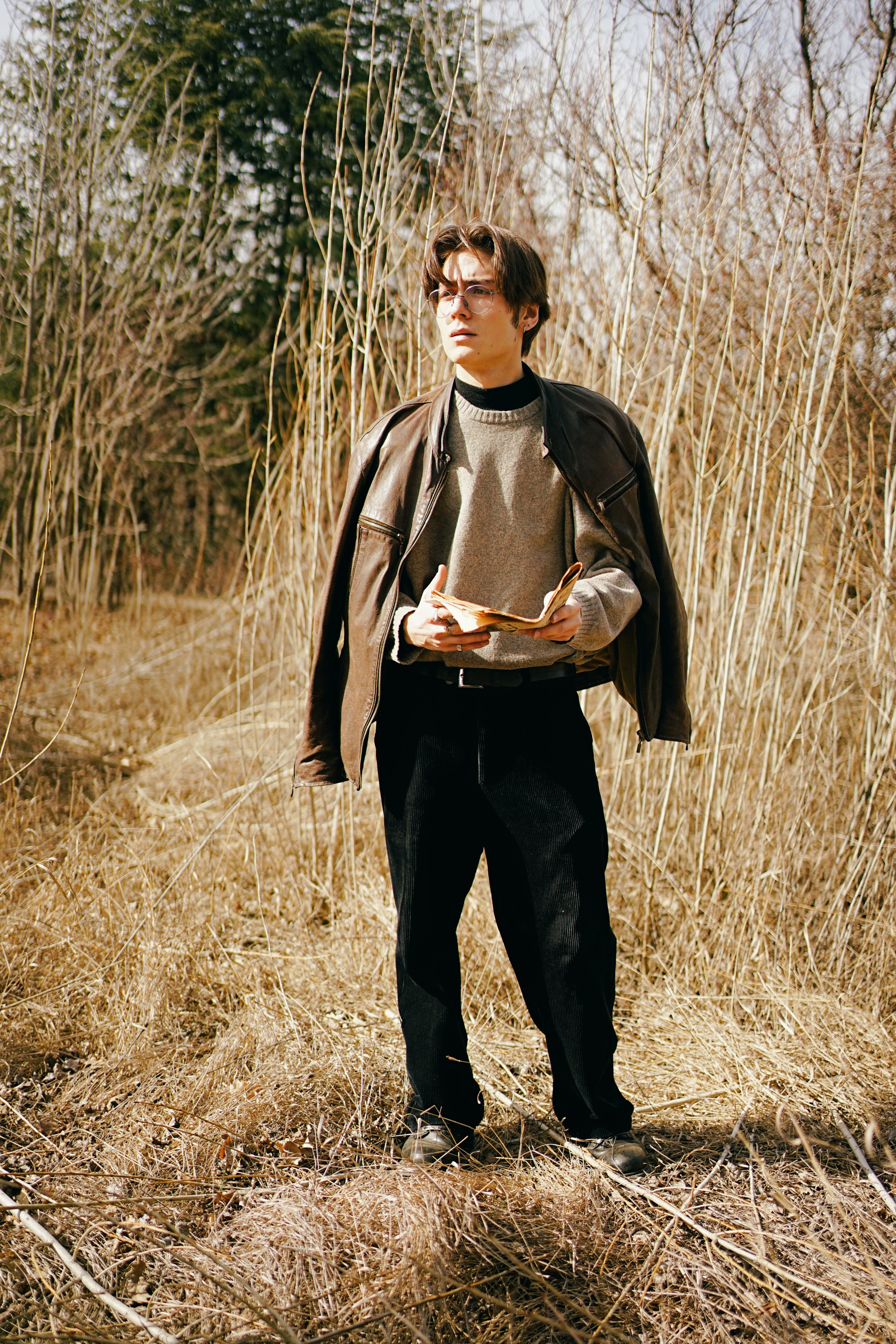 A stylish young man stands in a rural area of Ankara, showcasing modern fashion against a natural backdrop.