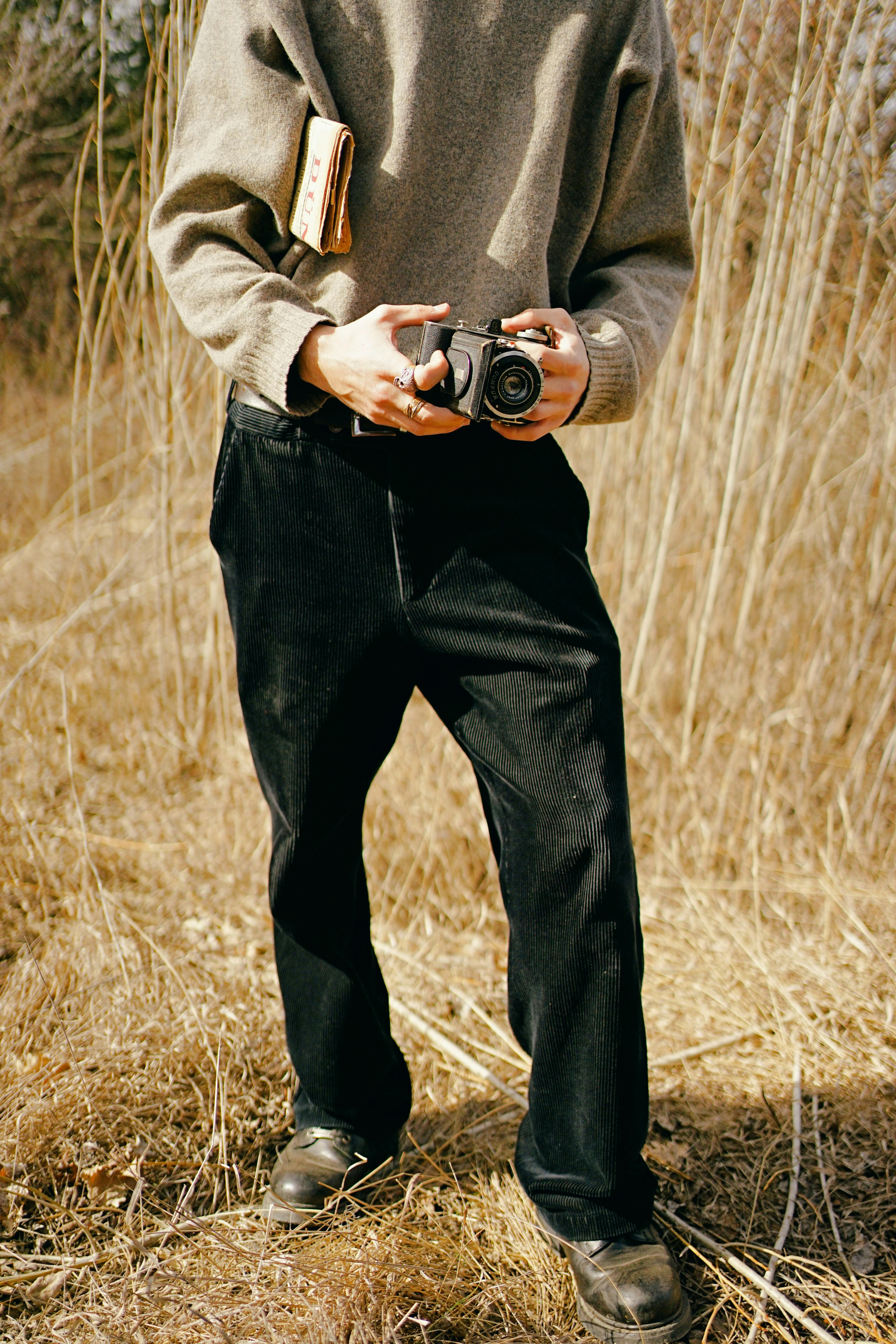 Man in black pants and gray sweater holding vintage camera in Ankara field.