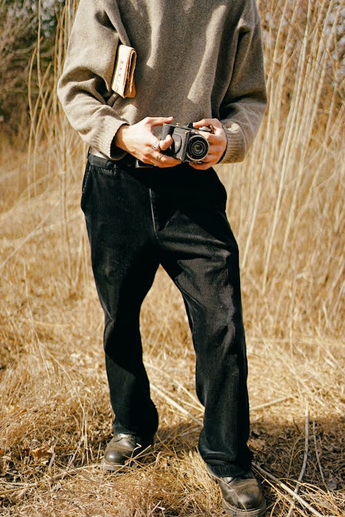 Man in a Gray Sweater and Black Corduroy Pants Holding a Vintage Camera