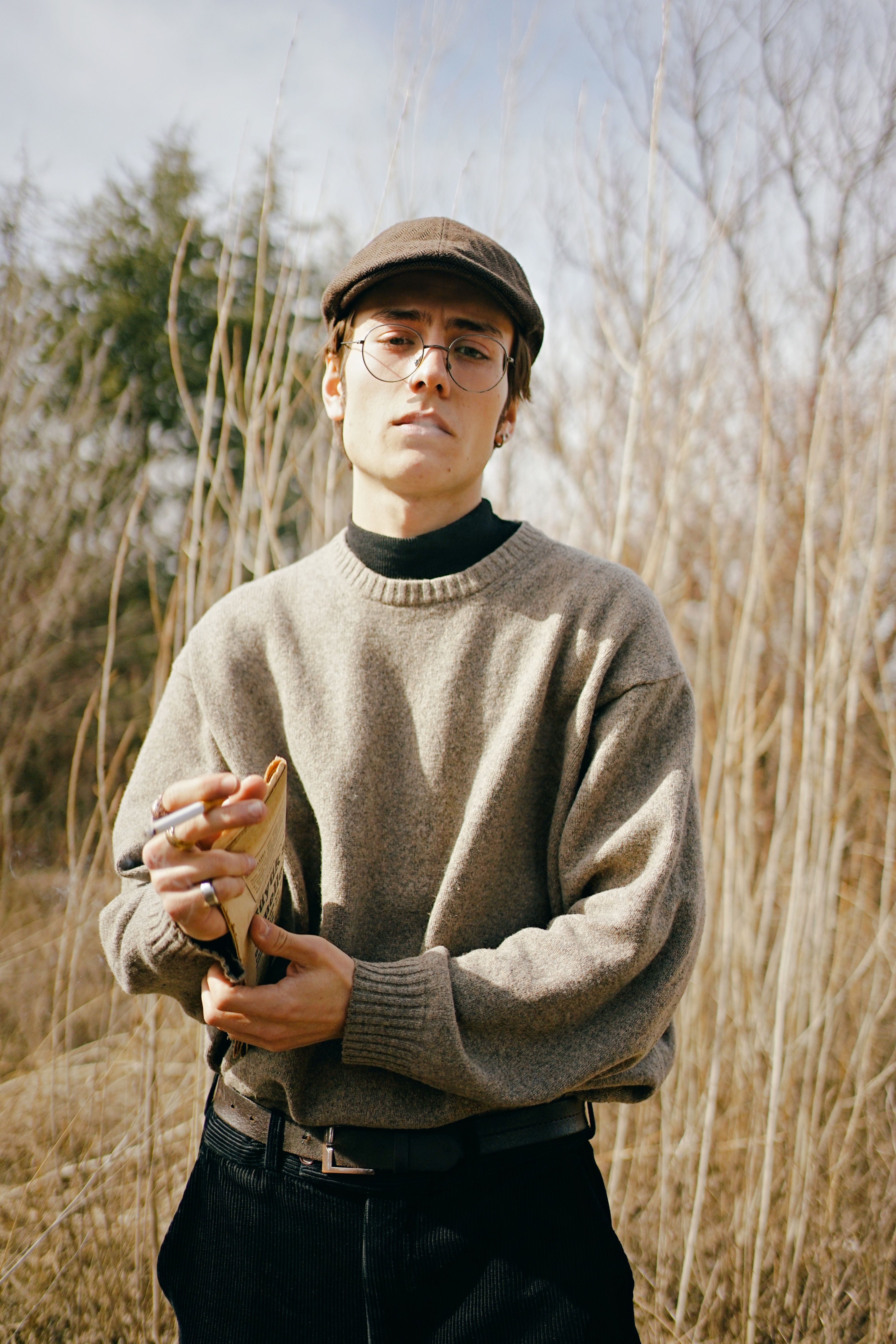Fashionable young man in Ankara wearing an ivy cap and glasses, captured in a rural setting.