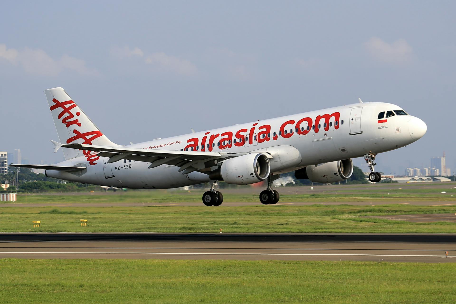 AirAsia Airbus A320 captured taking off from a busy airport runway on a clear day.