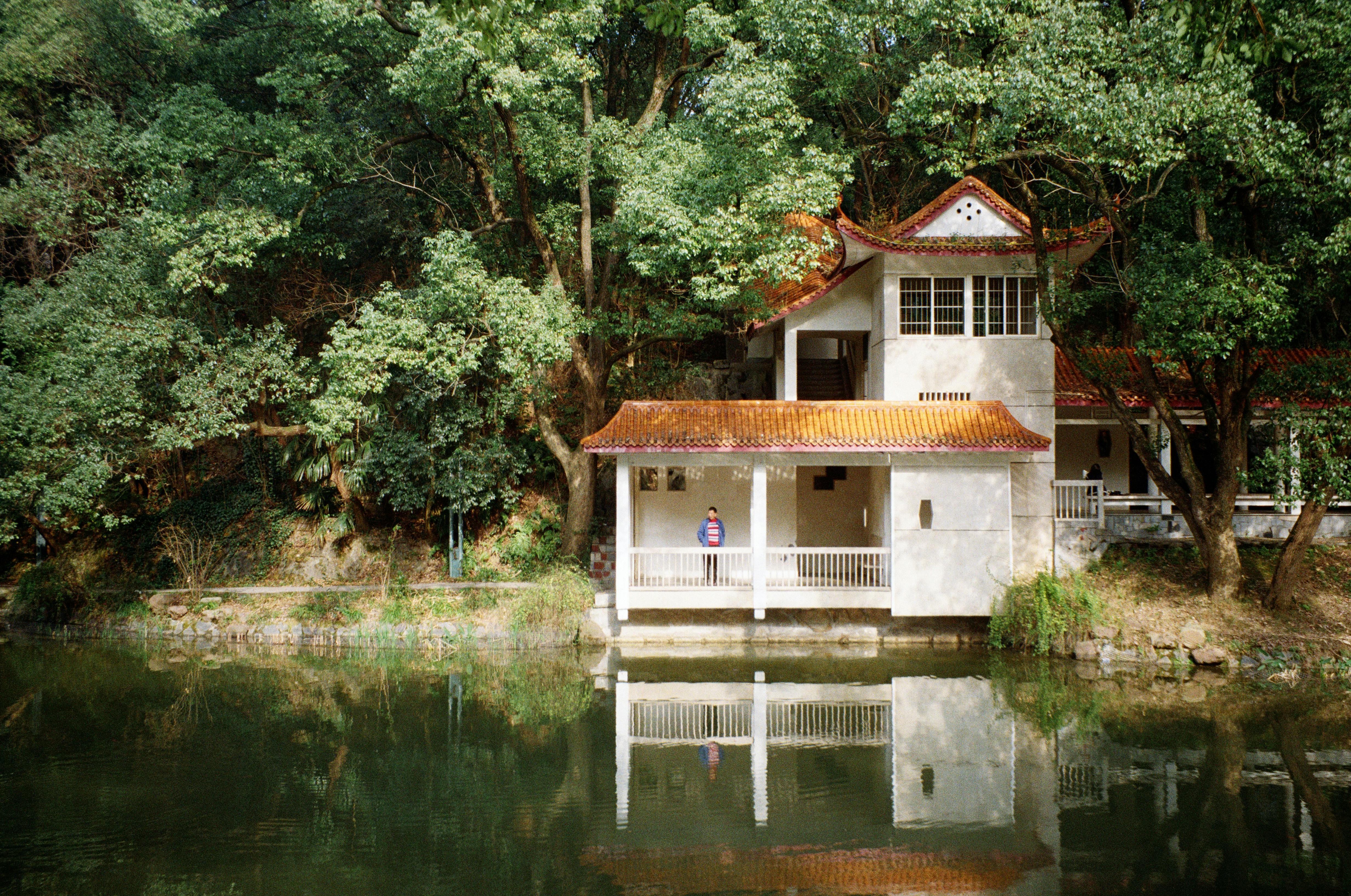 Serene scene of a Chinese-style building by a lake with lush trees and clear reflections.