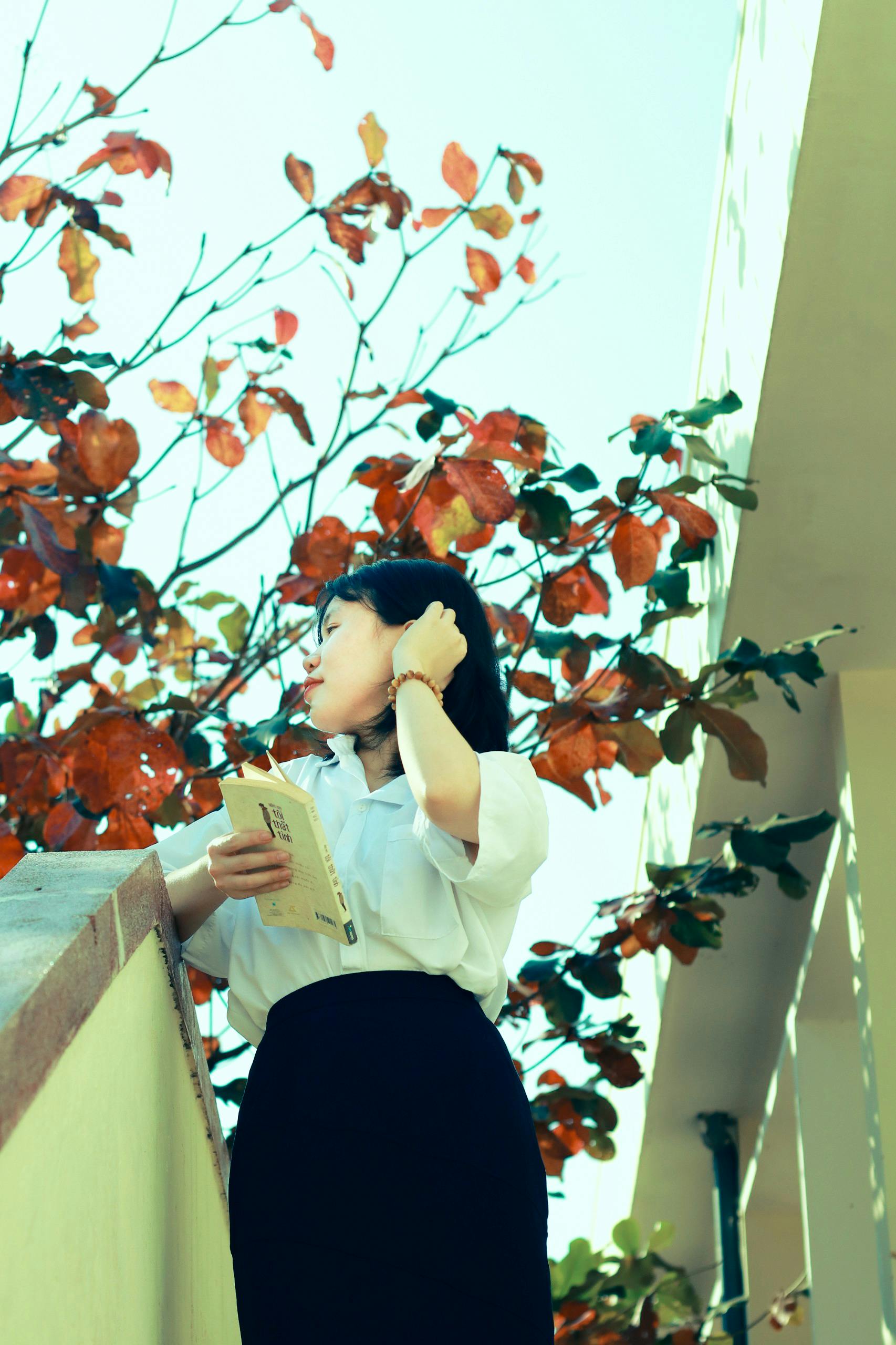 Portrait of an Asian woman in autumn, holding a book, wearing a white shirt.