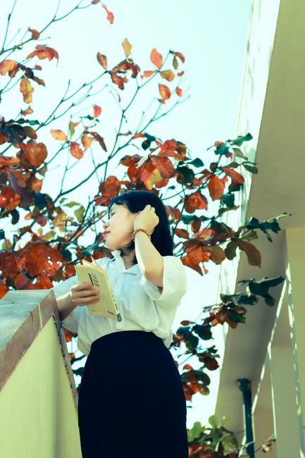 Portrait of an Asian woman in autumn, holding a book, wearing a white shirt.