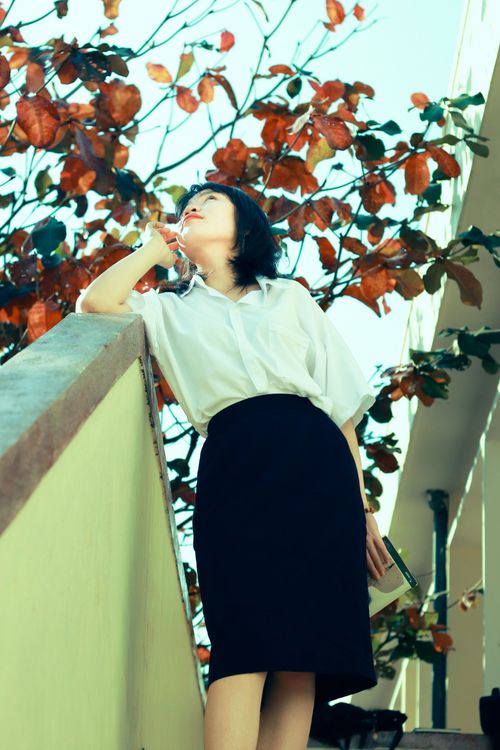 Free Elegantly dressed woman leans on staircase banister with autumn leaves in the background. Stock Photo