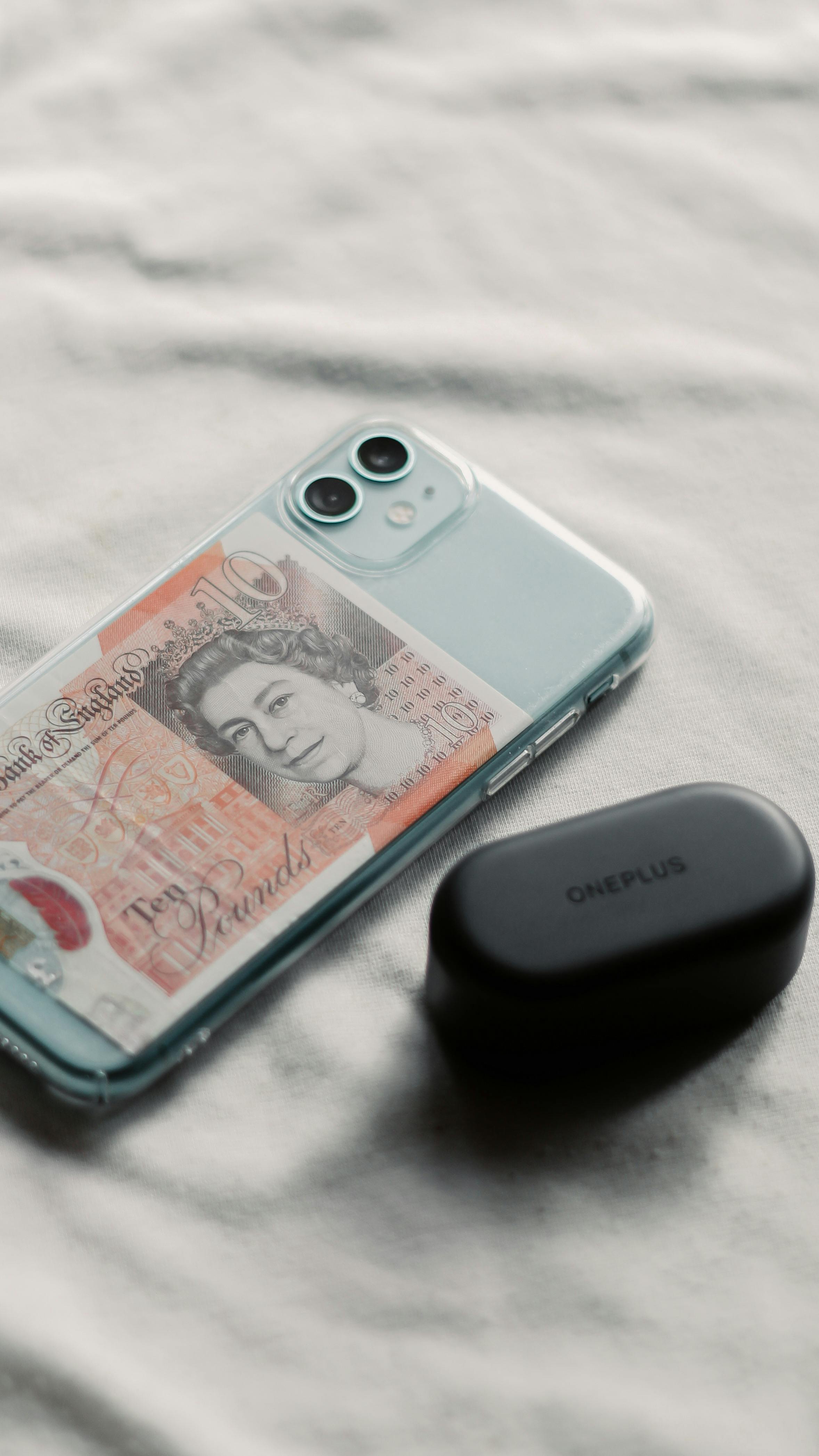 A smartphone with a British ten-pound note and OnePlus earbuds on a table.